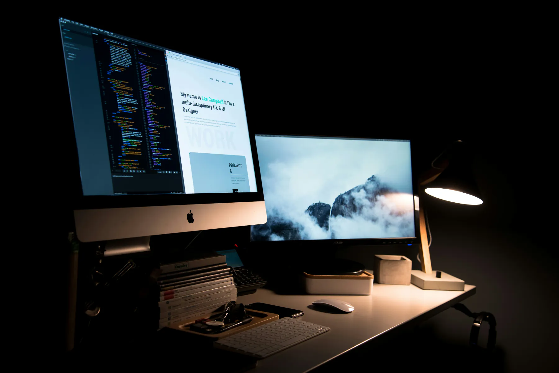 A dark desk lit by a lamp, with a monitor showing a website and its code side by side